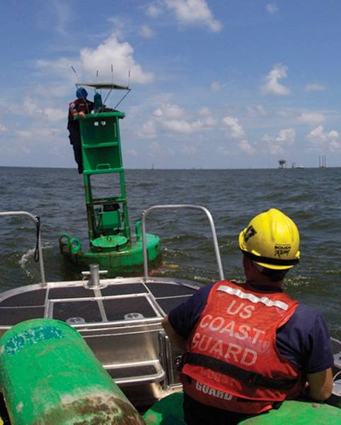 Ajudas aos membros da equipe de Navegação de Dulac, Louisiana, endireitam um painel solar que carrega o sistema de iluminação da ajuda. Foto da guarda costeira dos EU pelo oficial mesquinho a? A classe Thomas Atkeson.