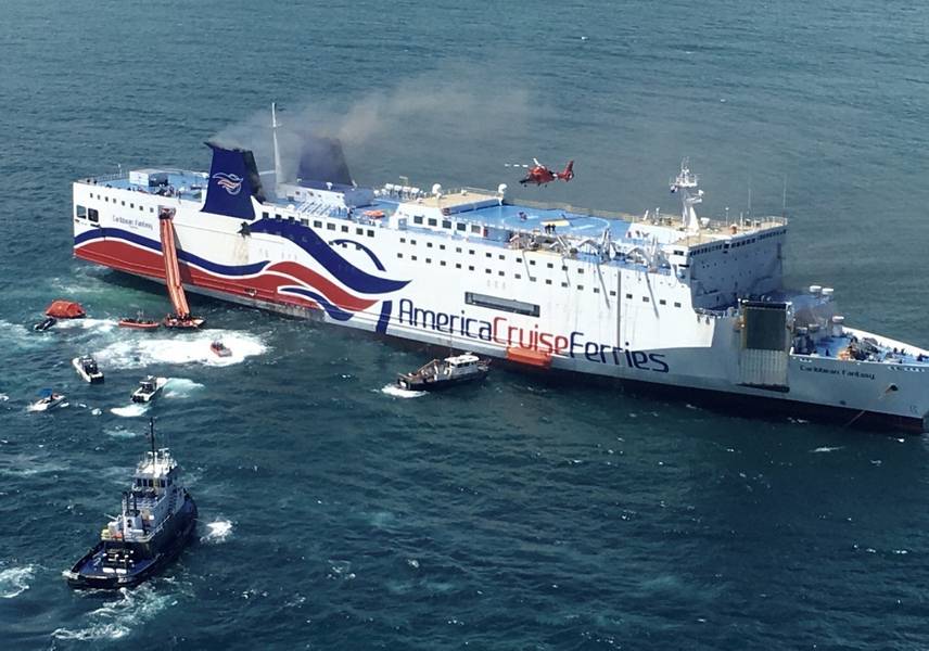 The Caribbean Fantasy's durante la etapa final de abandono, con su ancla de estribor hacia abajo. El humo gris sale de los dos embudos, y un helicóptero de la Guardia Costera está sobrevolando la cubierta superior de la nave. (Foto por la Guardia Costera de los Estados Unidos)