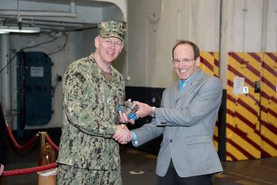 Don Hamadyk, director de investigación y desarrollo de Newport News Shipbuilding, presentó la primera pieza de metal impresa en 3D al Contralmirante Lorin Selby, ingeniero jefe y comandante adjunto del Comando de Sistemas Marinos Marinos para el diseño, la integración y la ingeniería naval de los buques durante una breve ceremonia en el USS Harry S. Truman (CVN 75). Foto por Matt Hildreth / HII.