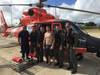 A MH-65 Dolphin helicopter crew from Coast Guard Air Station Barbers Point poses with a person they rescued Dec. 19, 2014, while on a routine patrol off Kauai. They were contacted by a tour helicopter on VHF radio channel 16 about an SOS marking written on the beach in the sand. (U.S. Coast Guard photo)
