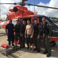 A MH-65 Dolphin helicopter crew from Coast Guard Air Station Barbers Point poses with a person they rescued Dec. 19, 2014, while on a routine patrol off Kauai. They were contacted by a tour helicopter on VHF radio channel 16 about an SOS marking written on the beach in the sand. (U.S. Coast Guard photo)