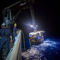 Crew members aboard a NOAA ship in 2016 use a crane to hoist a remotely operated vehicle (ROV) from the water at night. NOAA is seeking proposals for new ocean survey ships that can deploy a variety of equipment, including ROVs like the one pictured here. Credit: NOAA