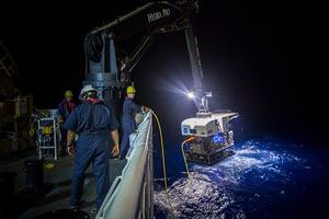 Crew members aboard a NOAA ship in 2016 use a crane to hoist a remotely operated vehicle (ROV) from the water at night. NOAA is seeking proposals for new ocean survey ships that can deploy a variety of equipment, including ROVs like the one pictured here. Credit: NOAA