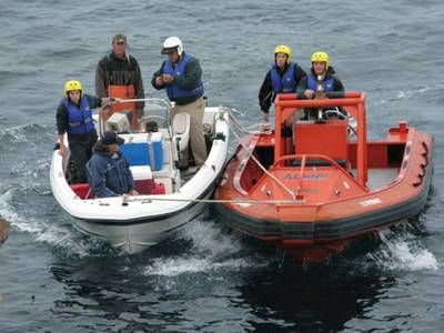 An Emergency Rescue Boat from the Cal Maritime training ship Golden Bear tows a stranded 17-ft. skiff back to the ship.  Golden Bear Chief Mate Bill Schmid (white helmet) and assistants (yellow helmets) assisted ship deck crew in lifting the stricken skiff aboard the ship along with the rescued fishermen for transport to San Francisco.  The Golden Bear diverted course on its final leg home from three-and-a-half months of training cruises to locate and rescue the fishermen after their outboard en