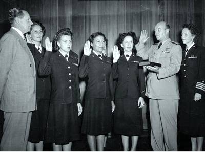 The first six enlisted women are: Front row: (left to right) Chief Yeoman Wilma J. Marchal, USN; Yeoman Second Class Edna E. Young, USN; Hospital Corpsman First Class Ruth Flora, USN Second row: (left to right) Aviation Storekeeper First Class Kay L. Langen, USN; (hidden behind the front row): Storekeeper Second Class Frances T. Devaney, USN; and Teleman Doris R. Robertson, USN. (NHHC Photo)