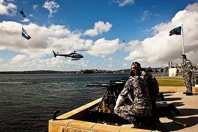 The Royal Australian Navy's Three Pound Saluting Gun Battery prepares to fire across Sydney Harbour as a Squirrel Helicopter decorated with International Fleet Review decals hovers off Garden Island Naval Base as a Seahawk helicopter flying a giant International Fleet Review Flag flys past.