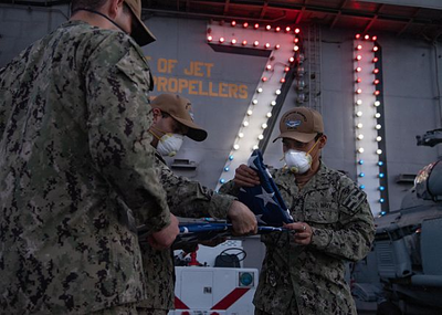 U.S. Sailors fold the American flag after evening colors on the flight deck of the aircraft carrier USS Theodore Roosevelt (CVN 71) April 24, 2020. (U.S. Navy photo by Kaylianna Genier)