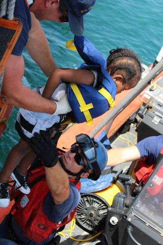A crewmember aboard the Coast Guard Cutter Valiant lowers a Haitian child to a boatcrew during a repatriation off the Coast of Haiti, June 16, 2015. (USCG photo)