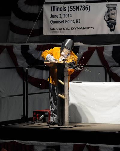 Electric Boat Quonset Point welder Michael Macomber inscribes the initials of First Lady Michelle Obama to a steel plate during the keel-laying ceremony for the submarine Illinois. (Photo: General Dynamics Electric Boat)