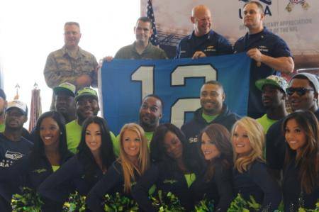 Master Chief Petty Officer Charles Lindsey (top right), command master chief of the Coast Guard 13th District, and Rear Adm. Richard Gromlich, commander of the Coast Guard 13th District, accept a Seattle Seahawks 12th Man flag from the Air Force 446th Airlift Wing (USCG photo by Katelyn Shearer)