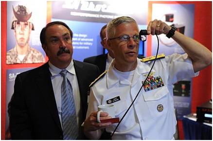 Rear Adm. Matthew Klunder, chief of naval research, tries out a low cost augmented reality head mounted display with SA Photonics general manager, Michael Browne, while touring the exhibit hall at the 2014 Navy Opportunity Forum. The forum is designed to facilitate interaction between small business and members of the acquisition community, lead system integrators, and first and second tier suppliers. (U.S. Navy photo by John F. Williams)