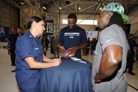 Petty Officer 1st Class Jennifer Gonzales, a yeoman assigned to the Coast Guard 13th District Auxiliary division, speaks with Seattle Seahawks players Terrance Parks (right) and Rashaun Allen (USCG photo by Katelyn Shearer)