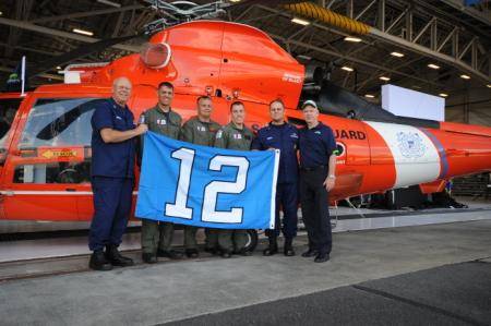 Rear Adm. Richard Gromlich (left), commander of the Coast Guard 13th District; retired Coast Guard aviator Michael Flood (right), a member of the Seattle Seahawks organization; Master Chief Petty Officer Charles Lindsey, command master chief of the Coast Guard 13th District and an aircrew from Coast Guard Air Station Port Angeles, Wash., pose for a photo with a Seattle Seahawks 12th Man flag in front of an MH-65 Dolphin helicopter (USCG photo by Katelyn Shearer)